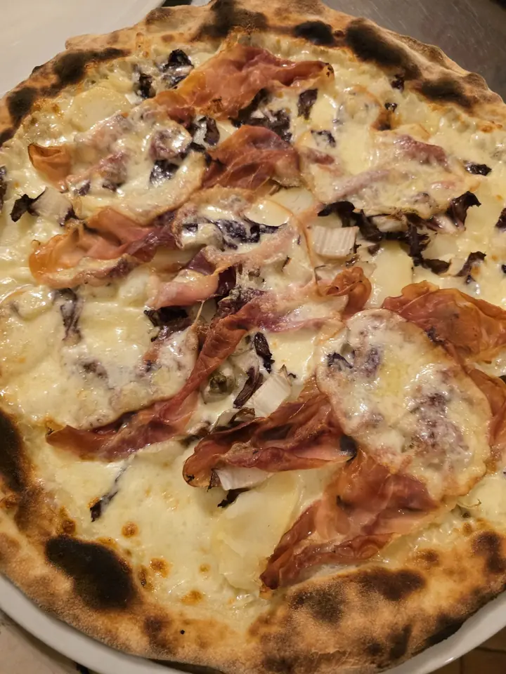 Pizza bianca con prosciutto crudo, radicchio e formaggio fuso, con il bordo bruciacchiato dal forno a legna